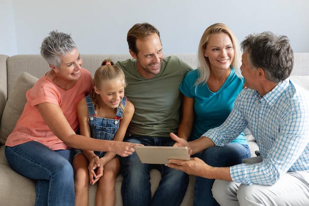 Foto glimlachende blanke grootouders op de bank met kleindochter en haar ouders die naar tablet kijken