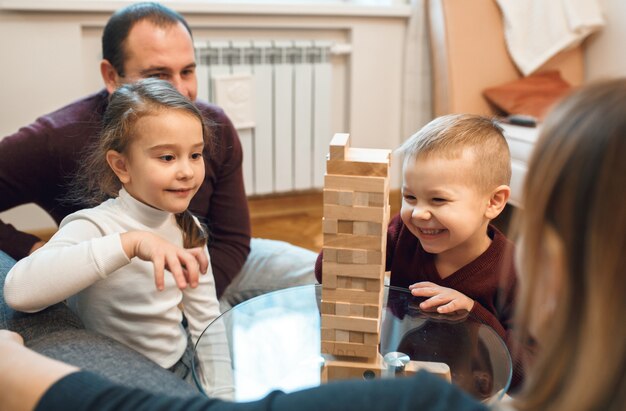 Glimlachende blanke jongen speelt jenga met zijn grotere zus terwijl hun ouders trots kijken