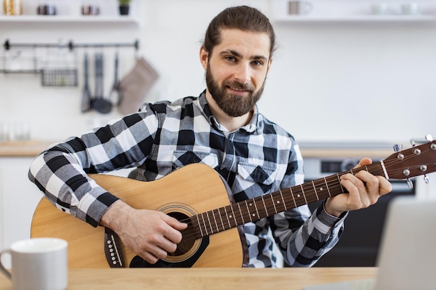 Glimlachende blanke man leert een instrument spelen met behulp van online lessen op een laptop