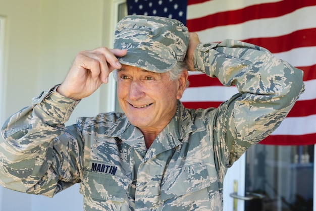 Glimlachende blanke senior legermilitair in camouflagekleding met pet tegen de vlag van amerika