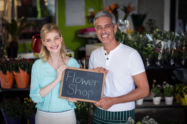 Glimlachende bloemisten die het teken van de bloemwinkel op lei in bloemwinkel houden