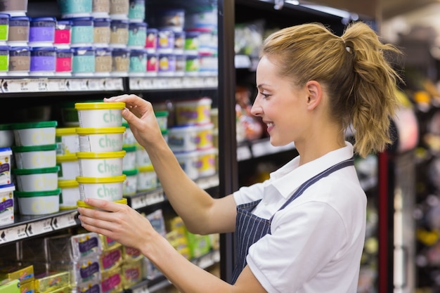 Glimlachende blonde arbeider die producten in plank neemt