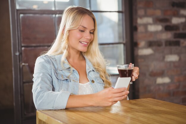 Glimlachende blonde het drinken koffie en het gebruiken van smartphone