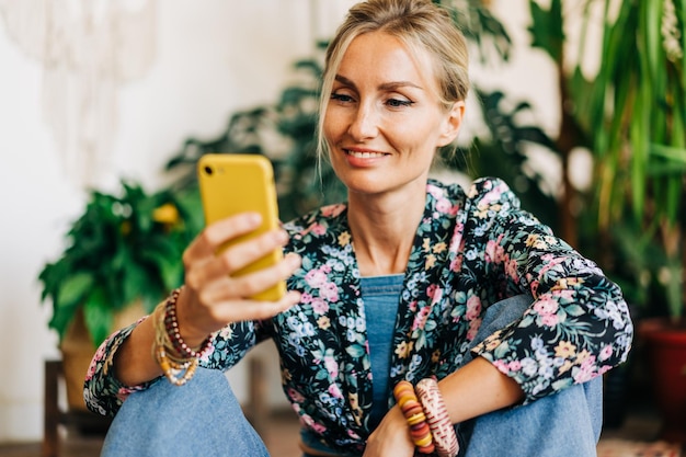 Glimlachende blonde kijkt naar het scherm van een mobiele telefoon en leest een bericht