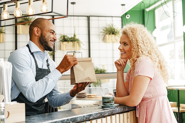 Glimlachende blonde vrouw die met een ober van een coffeeshop spreekt