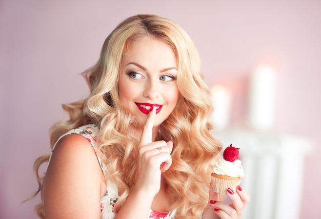 Glimlachende blonde vrouw die smakelijke cupcake houdt