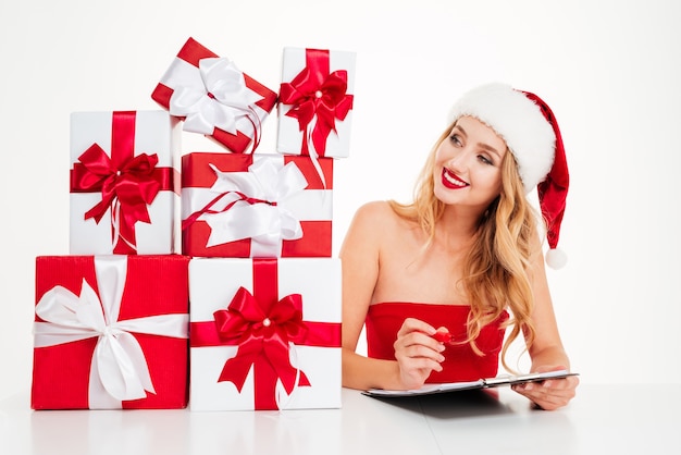 Glimlachende blonde vrouw in kerstmuts met veel geschenkdozen