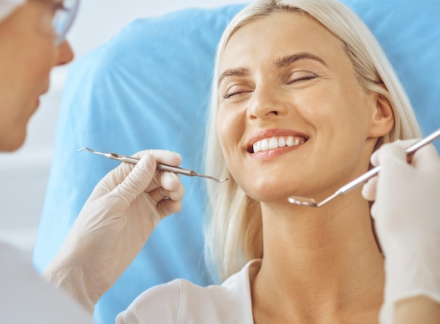 Glimlachende blonde vrouw onderzocht door een tandarts in een tandheelkundige kliniek.