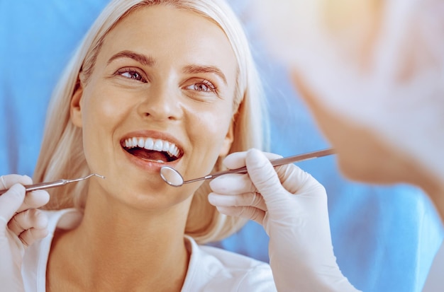 Glimlachende blonde vrouw onderzocht door tandarts bij tandheelkundige kliniek Gezonde tanden in geneeskunde concept