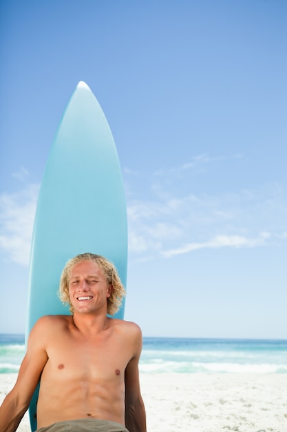 Glimlachende blondemens die op het strand met zijn surfplank naast hem zonnebaden