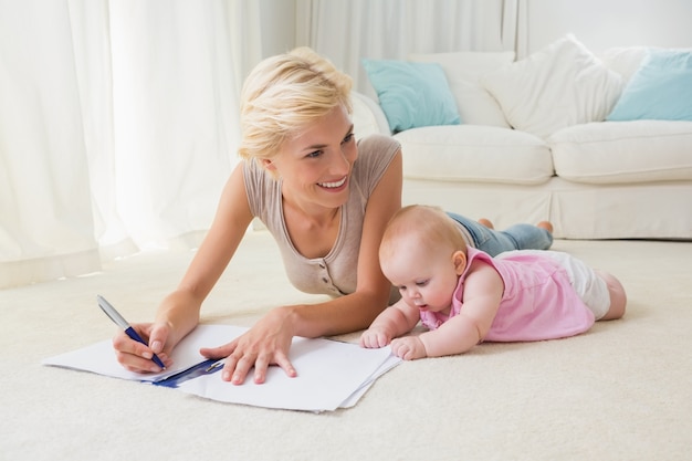 Glimlachende blondemoeder met haar babymeisje die op een voorbeeldenboek schrijven