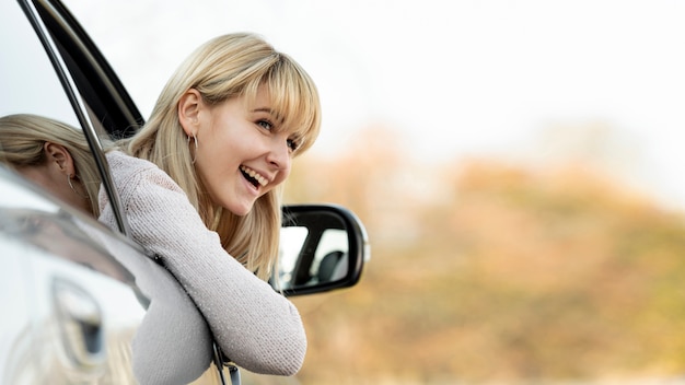 Foto glimlachende blondevrouw die haar hoofd nemen uit vensterauto