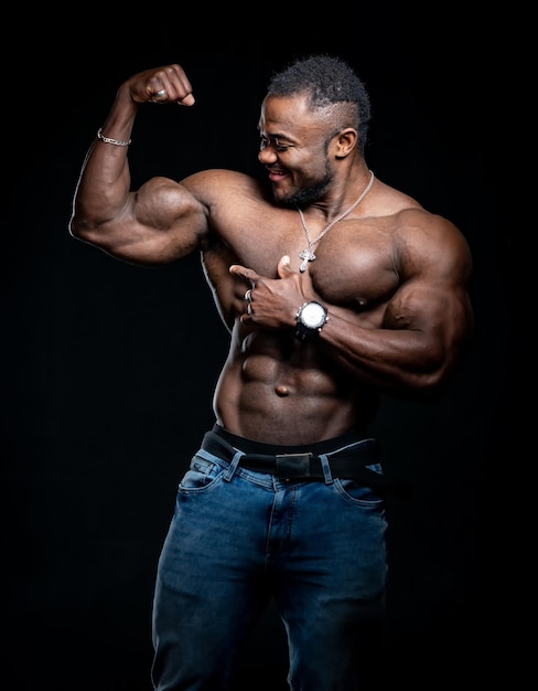 Glimlachende bodybuilder met sterk lichaam poseert voor de camera met naakte torso. Atleet die sterke handen toont. Zwarte achtergrond.