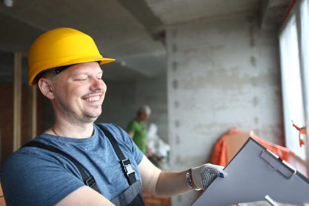 Glimlachende bouwer die klembord vasthoudt en het benodigde werkmateriaal voor renovatie opschrijft