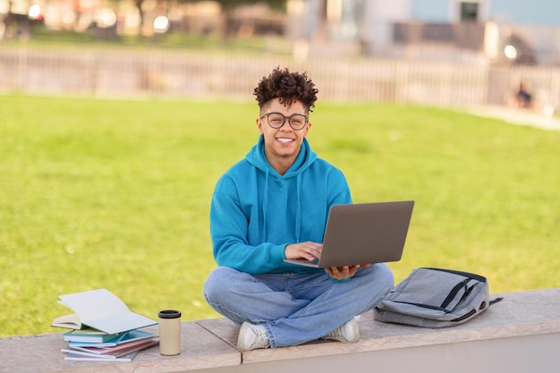 Foto glimlachende braziliaanse student die op een laptop surft en buiten zit.