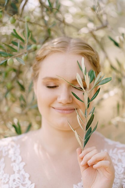 Glimlachende bruid staat met gesloten ogen met olijftak in de hand