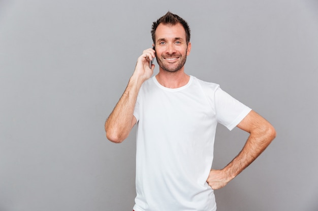 Glimlachende casual man praten aan de telefoon geïsoleerd op een grijze achtergrond