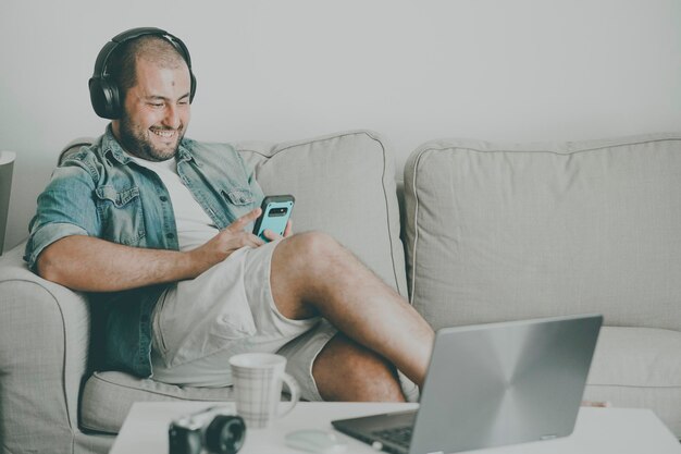 Foto glimlachende casual uitziende man die op de bank zit en een mobiele telefoon gebruikt