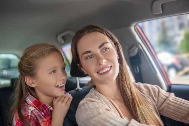 Glimlachende dochter in gesprek met haar moeder vanaf de achterbank van de auto