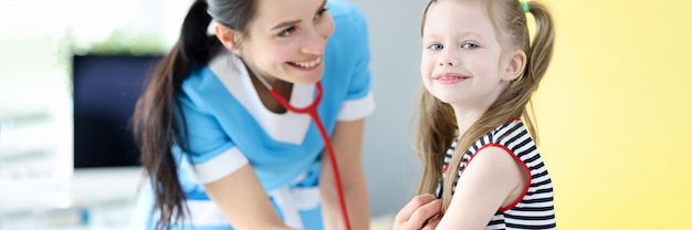 Glimlachende dokter luistert met een stethoscoop naar de ademhaling van een klein meisje