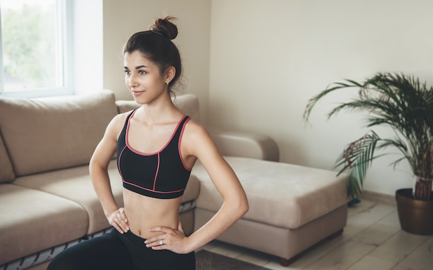 Glimlachende donkerbruine vrouw in sportkleding die huisfitness op de vloer doet