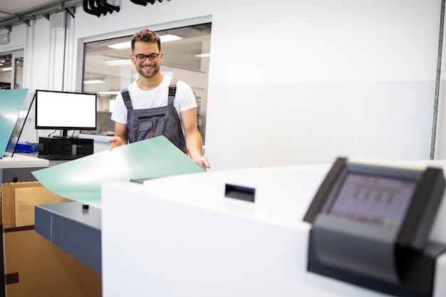 Glimlachende drukker die de computer bedient om de machine in de drukkerij te borduren.