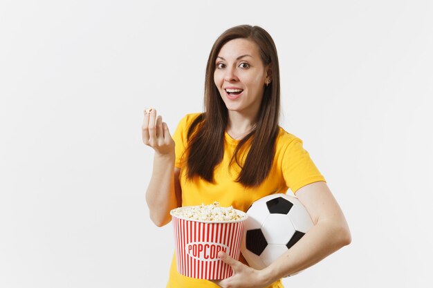 Glimlachende Europese jonge vrouw, voetbalfan of speler in geel uniform met voetbal, emmer popcorn geïsoleerd op een witte achtergrond. Sport, voetbal, juichen, fans mensen lifestyle concept.