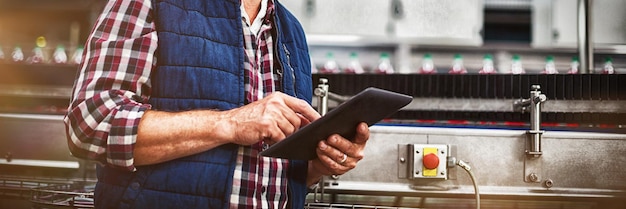 Glimlachende fabrieksarbeider die digitale tablet in de fabriek gebruikt