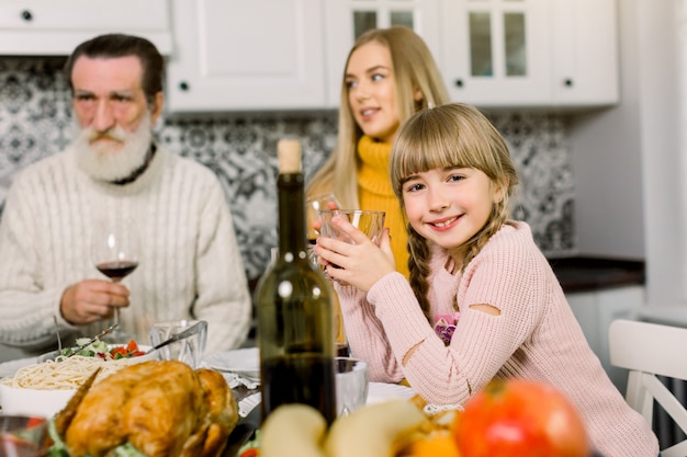 Glimlachende familie die diner heeft thuis, nadruk op weinig glimlachend meisje dat glas met sap houdt