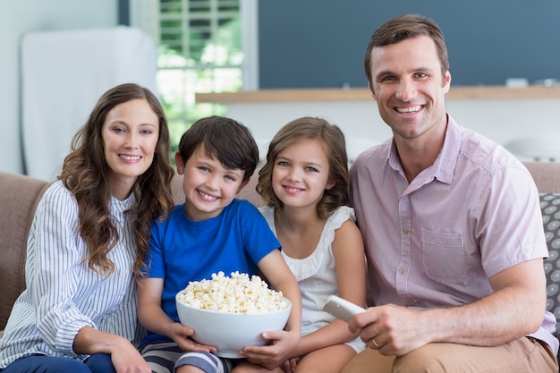 Glimlachende familie die op TV letten en thuis popcorn in woonkamer eten