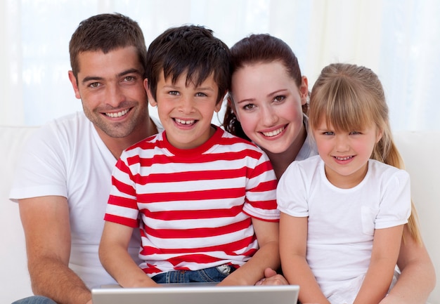 Glimlachende familie die thuis laptop met behulp van