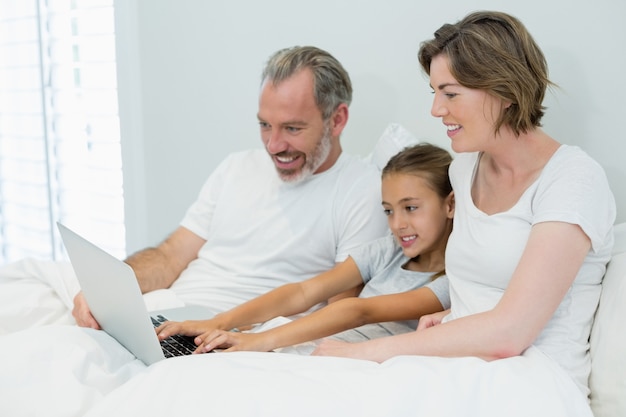 Glimlachende familie met laptop op bed in de slaapkamer