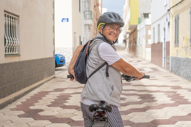 Glimlachende fietser senior vrouw met fietshelm die in stedelijke straat loopt Gezonde levensstijl en duurzaam mobiliteitsconcept