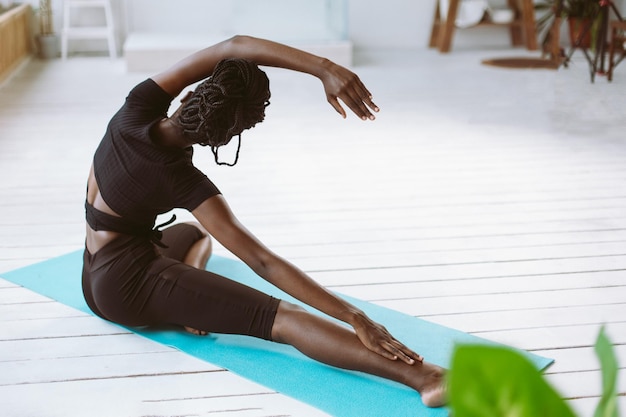 Glimlachende flexibele sportieve blote voeten donkere huid interraciale vrouw stretch doen yoga fitness oefeningen op mat thuis