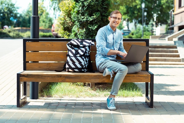 Glimlachende freelancer die zich druk voelt terwijl hij zijn werk afmaakt terwijl hij op de bank zit