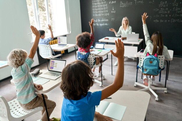 Glimlachende gelukkige leraar die wiskundeles heeft met schoolkinderen die bij bureau zitten