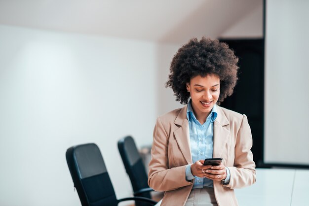 Glimlachende gemengd ras zakenvrouw met behulp van slimme telefoon in de vergaderzaal.