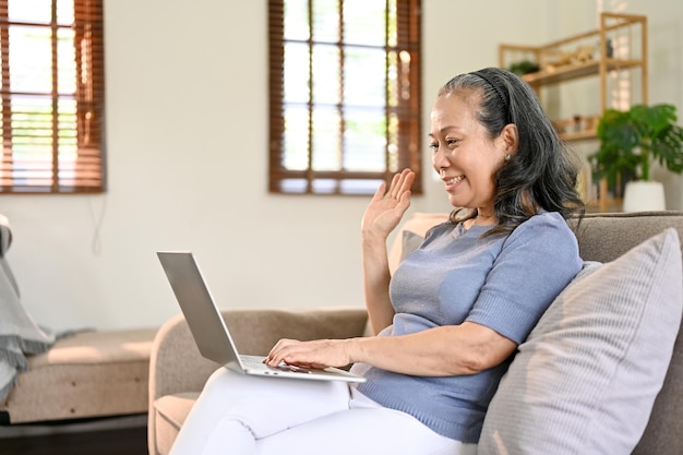 Glimlachende gepensioneerde vrouw van Aziatische leeftijd die met haar dochter praat via een videogesprek via een laptop