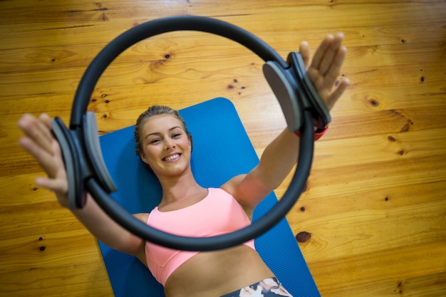 Glimlachende geschikte vrouw die met pilatesring op mat uitoefent