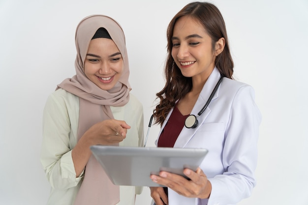 Glimlachende gesluierde vrouw met wijzende hand en gelukkige mooie vrouwelijke arts terwijl ze samen tablet gebruiken