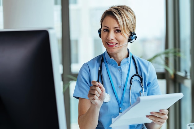 Glimlachende gezondheidswerker die een headset draagt terwijl hij in een medisch callcenter werkt en met patiënten praat