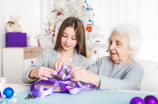 Glimlachende grootmoeder met kleindochter die cadeaus versieren met Kerstmis