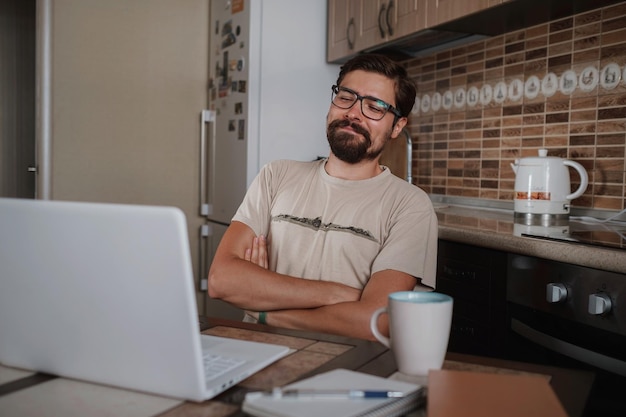 Glimlachende hipster freelancer hand in hand achter hoofd zittend aan bureau achter laptop