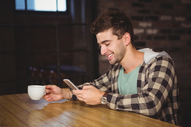 Glimlachende hipster het drinken koffie en het gebruiken van smartphone