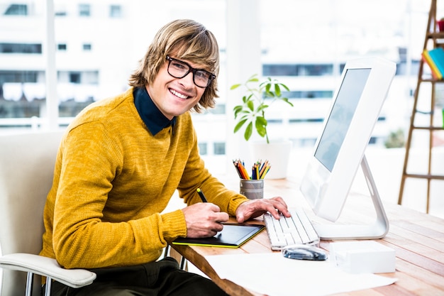 Glimlachende hipster zakenman die tablet grafisch in zijn bureau gebruiken