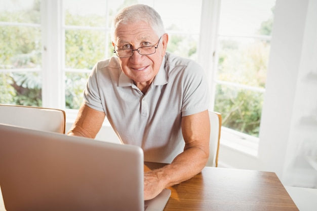 Glimlachende hogere mens die laptop thuis met behulp van