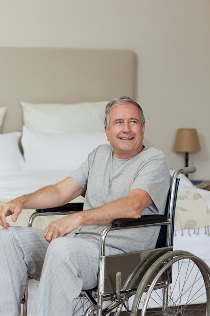 Glimlachende hogere mens in zijn rolstoel thuis