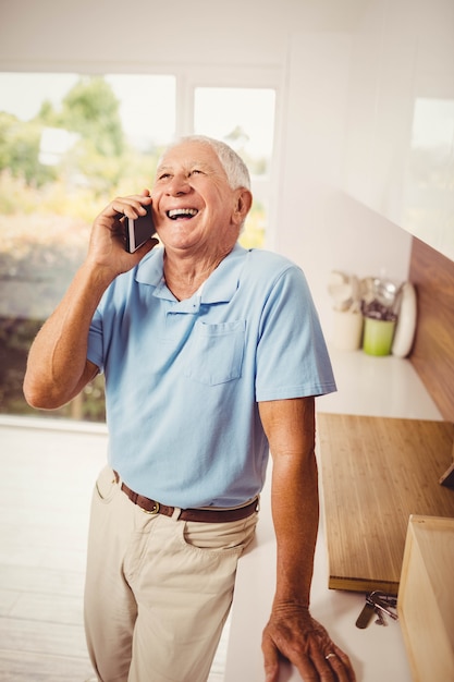 Glimlachende hogere mens op een telefoongesprek in de keuken