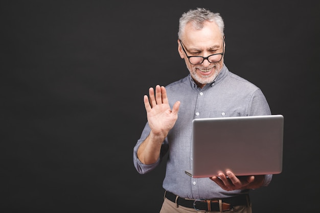 Glimlachende hogere oude oude zakenman in oogglazen die laptop computer voor praatje met behulp van