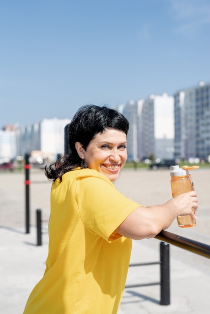 Glimlachende hogere vrouw die rust na training buiten op de bars van het sportveld heeft